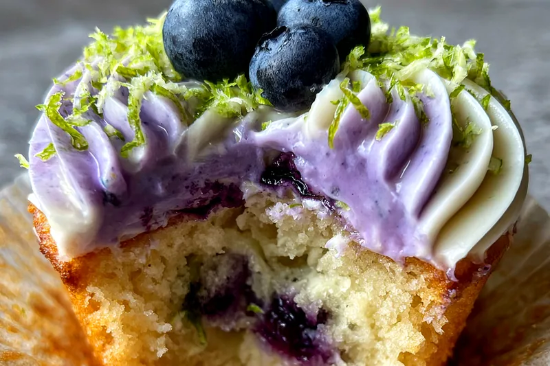 An image showing the process of frosting Blueberry Lime Cheesecake Cupcakes with cream cheese frosting.
