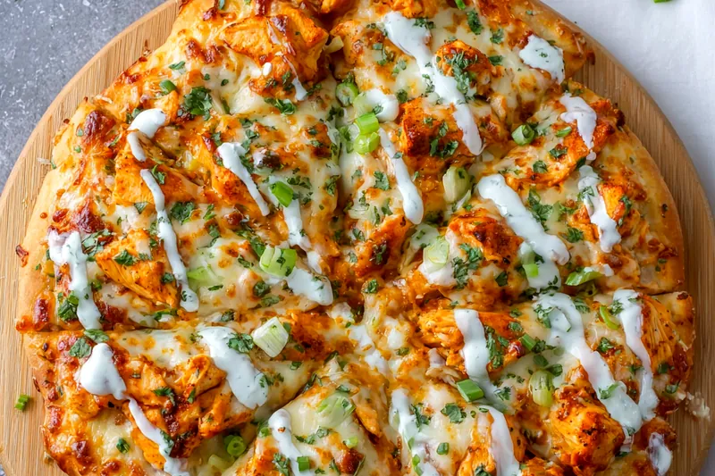 Buffalo chicken pizza ingredients including diced raw chicken, buffalo sauce, ranch dressing, mozzarella cheese, blue cheese, and fresh celery arranged on a marble countertop