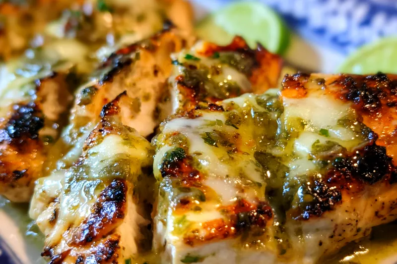 Raw chicken breasts with colorful spice blend, jar of salsa verde, shredded pepper jack cheese, and lime wedges arranged on a wooden board