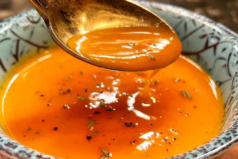 Whisking orange yum yum sauce in a clear glass bowl, showing the creamy orange-tinted mixture with visible orange zest flecks